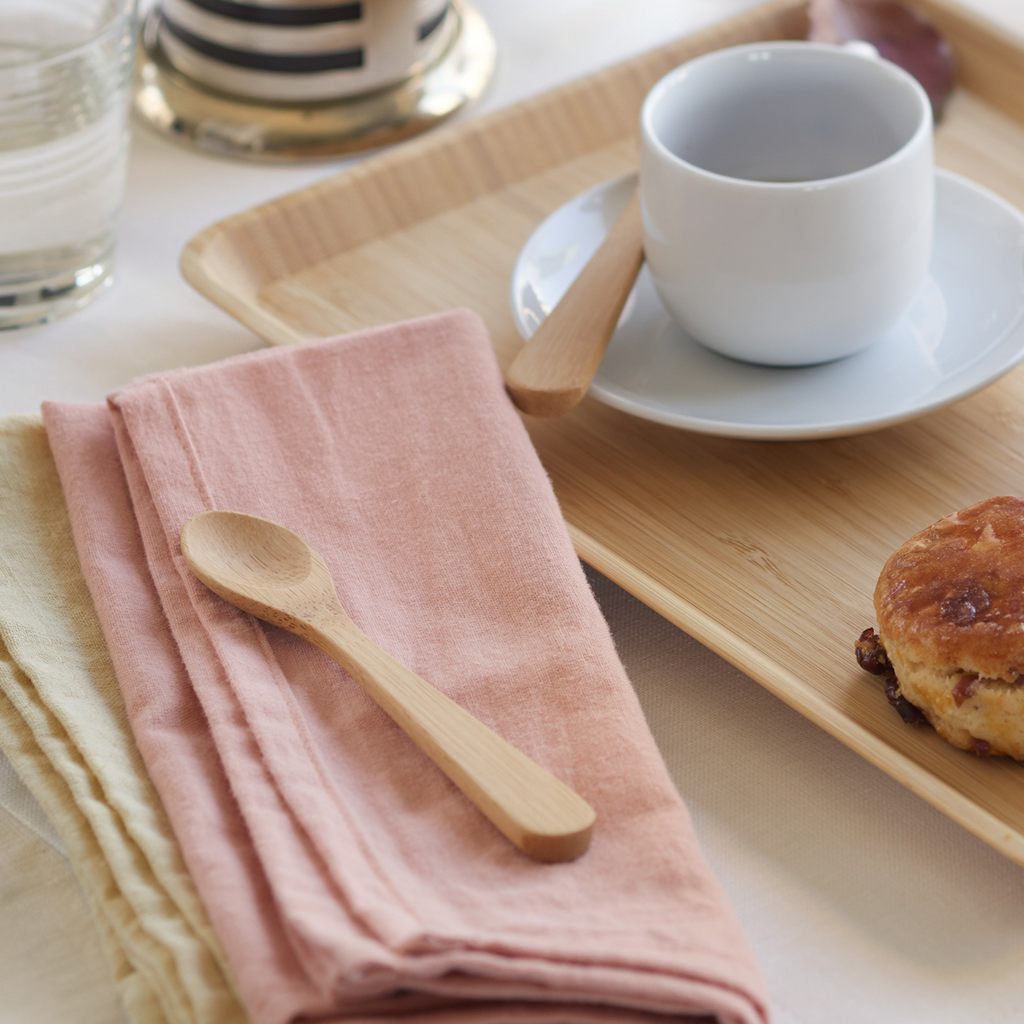 Bamboo teaspoon on a pink napkin next to a tray of tea and scones.