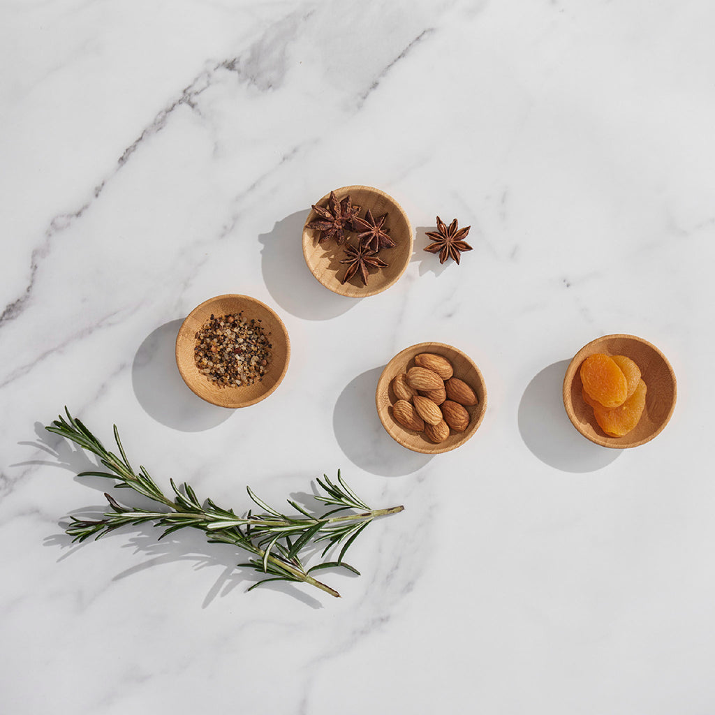 a set of 4 small condiment cups are shown on a marble background. There is dried fruit, nuts, and spices in the cups.