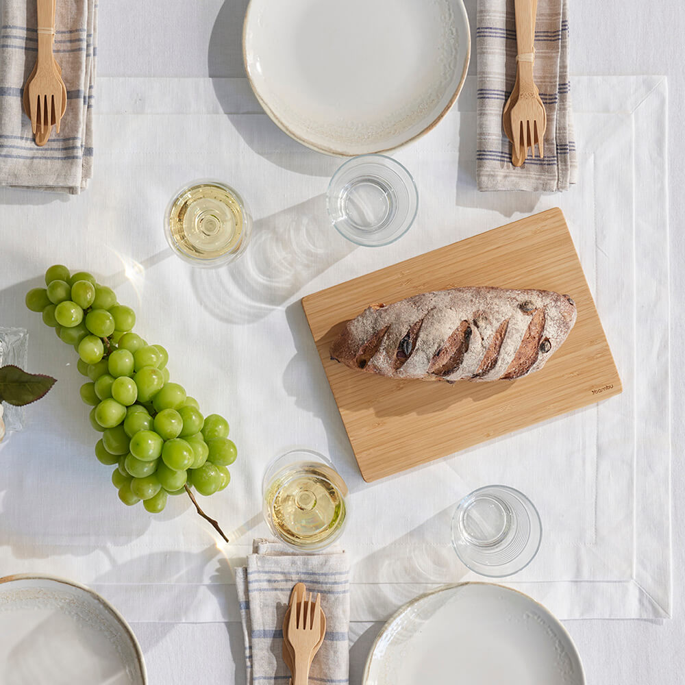 A Medium Undercut Series Cutting Board rests on a dining table. A loaf of bread is on the board. - bambu