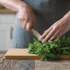 A person in a blue striped apron chops fresh herbs on a Large Undercut Series Cutting Board - bambu