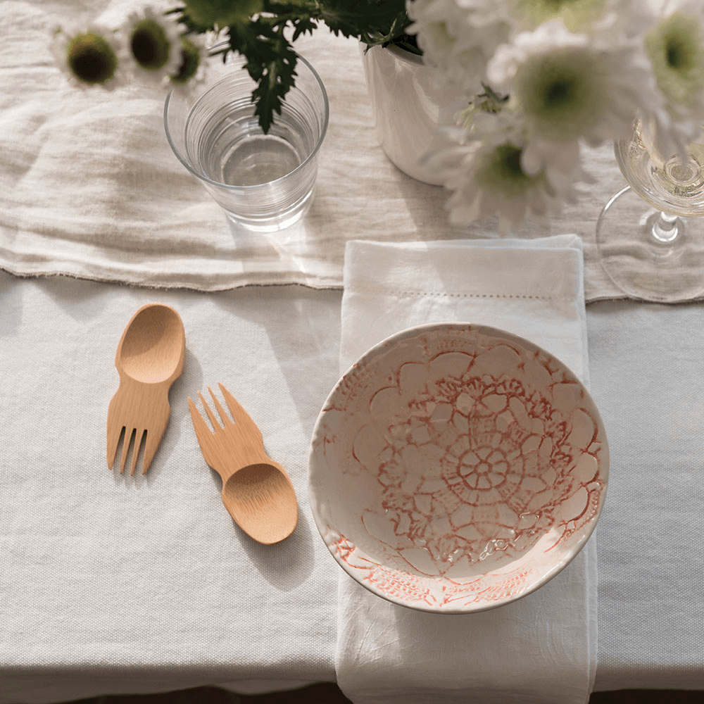 A pair of Bamboo Sporks lay near a floral patterned ceramic bowl on the table.