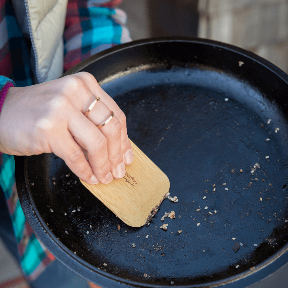 A bamboo pot scraper is used to clean a cast iron cooking pan
