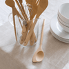A Spoontula lays next to a glass utensil crock that is filled with other bamboo cooking tools.