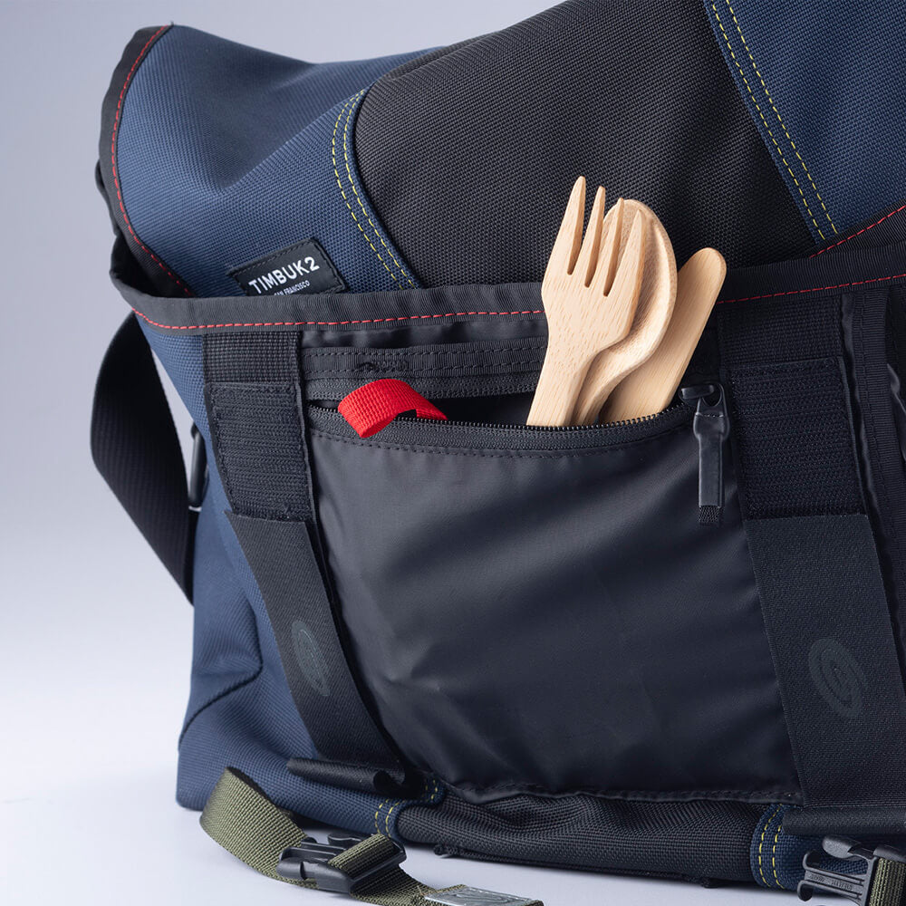 A set of Bamboo Cutlery - Spoon, Knife & Fork, peek from a pocket inside of a messenger bag.