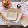 A 7" square and 9" square Veneerware plate are on a patterned table runner. A loaf of bread and a bowl of grapes are next to the plates.