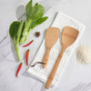 A bamboo rice paddle and wok spatula lay next to fresh vegetables, ready for cooking.